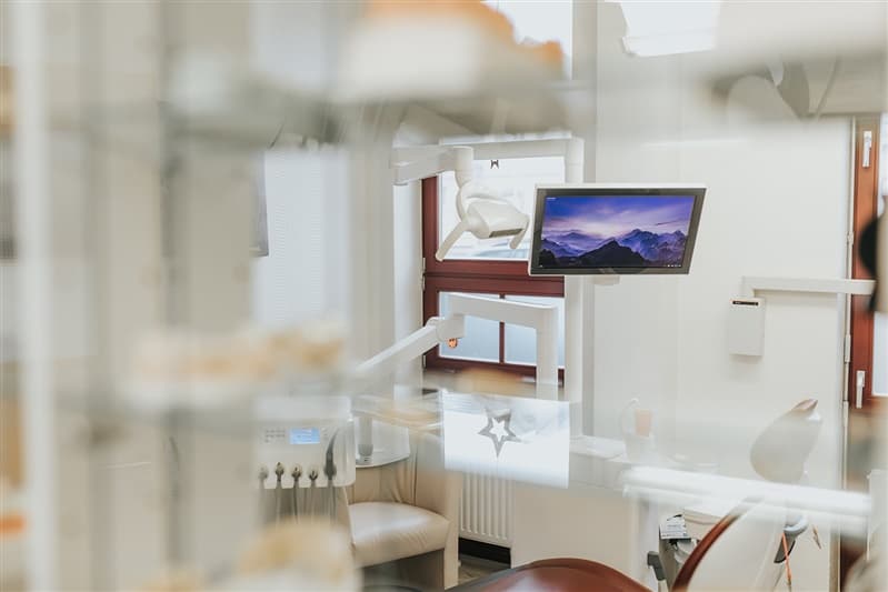 Behandlungszimmer mit Bildschirm und Behandlungsleuchte, aufgenommen durch eine Vitrine